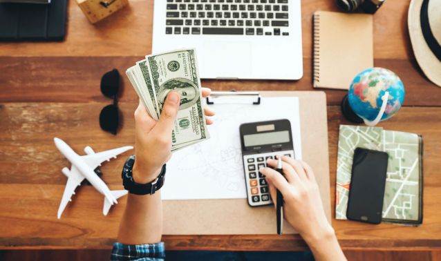 Hands holding cash and using a calculator and laptop.