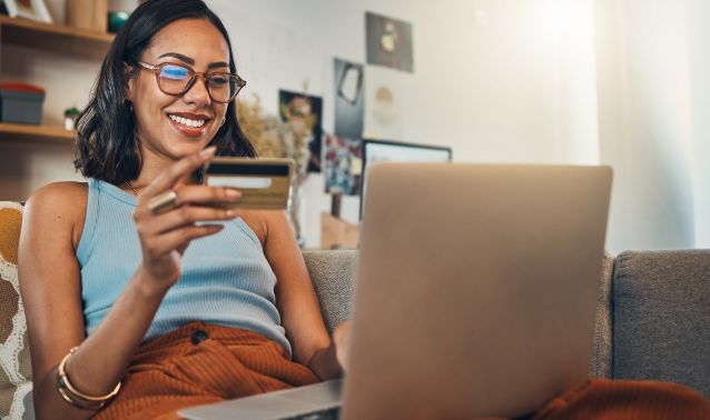 A woman looking at a credit card and her laptop.