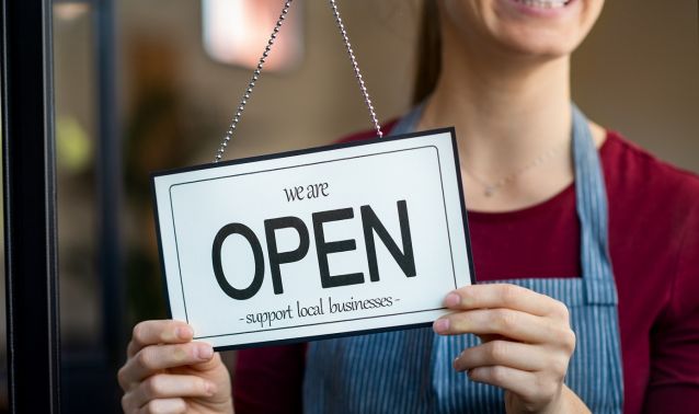 A woman holding a 'We're Open' sign.