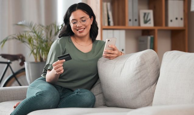 A woman holding her credit card looking at her phone.