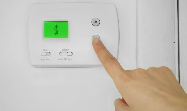 A finger lowering the heat on a thermostat.