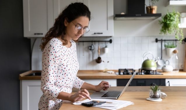 A woman working on a laptop in her kitchen.