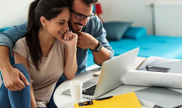 two people smile while doing taxes on a laptop