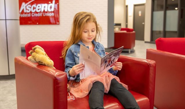 Young girl sitting inside an Ascend Federal Credit Union branch reading