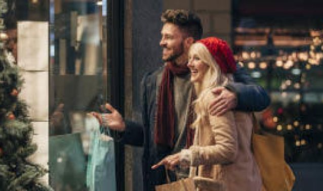 A couple looks through a window while holiday shopping.