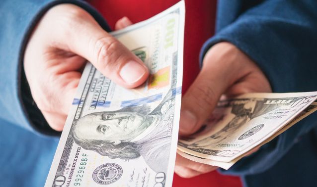 Person holding money and handing over a one hundred dollar bill