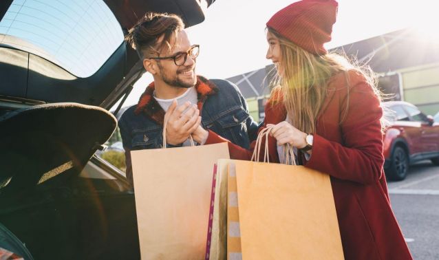 Couple putting shopping bags into trunk of car while smiling