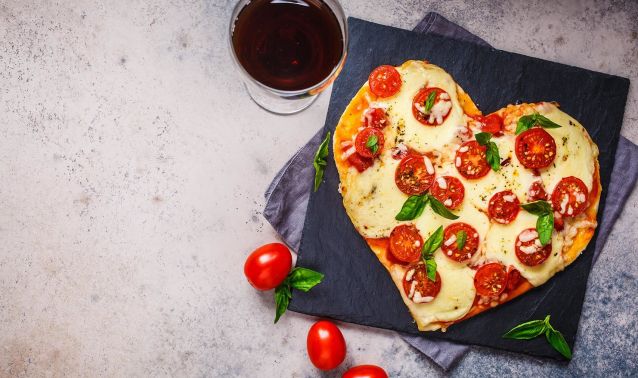 A pizza shaped like a heart with a glass of wine.