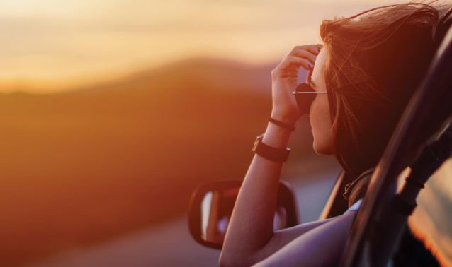 Young woman looking out of her car at sunset