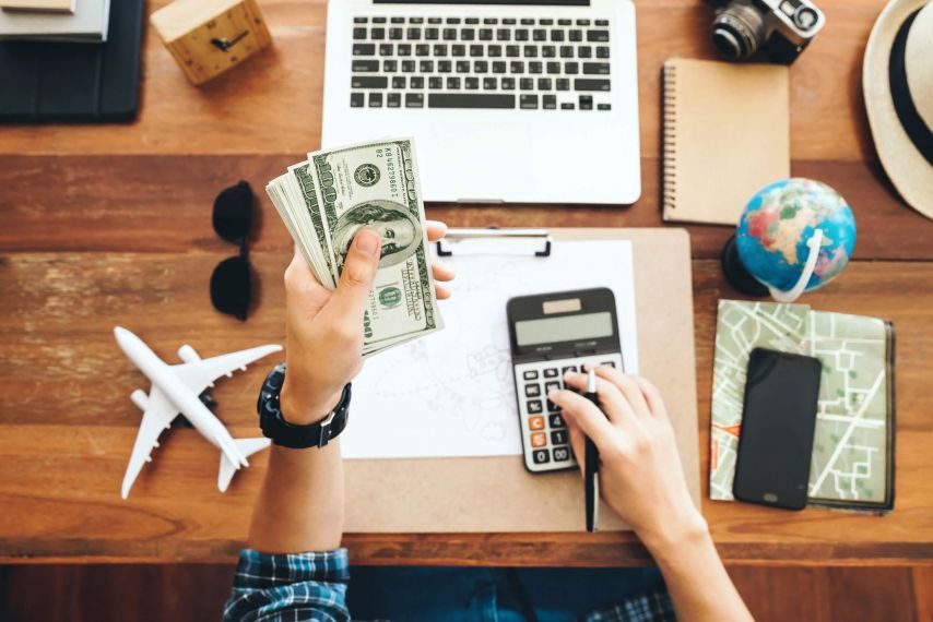 Hands holding cash and using a calculator and laptop.