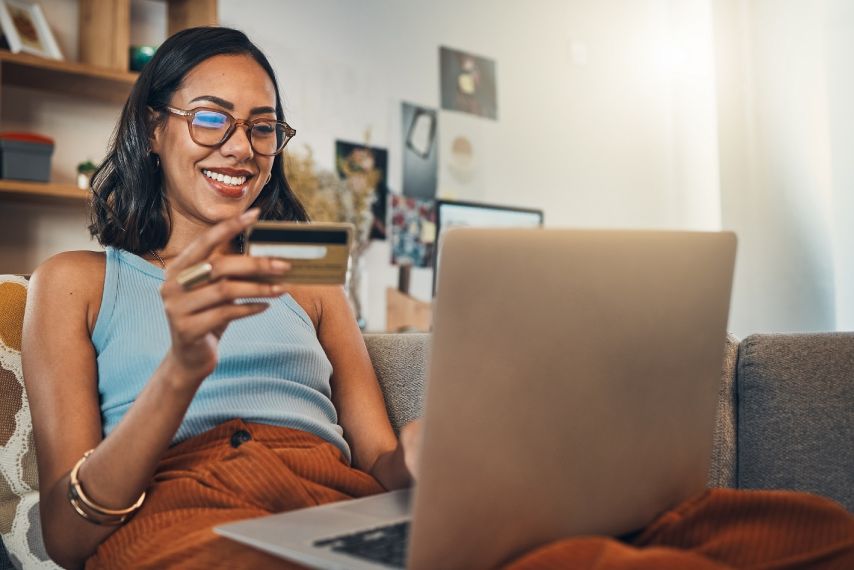 A woman looking at a credit card and her laptop.