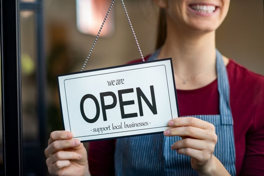 A woman holding a 'We're Open' sign.