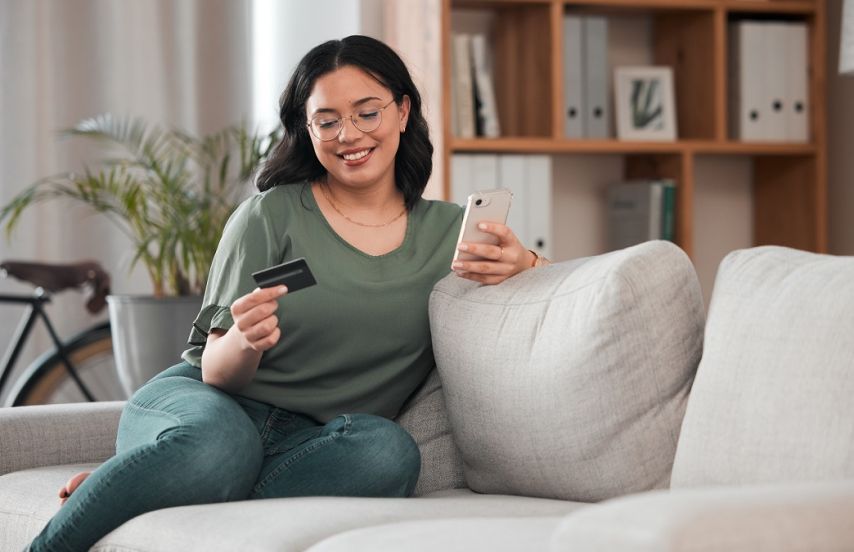 A woman holding her credit card looking at her phone.