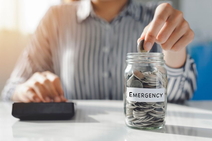 A person putting money into an emergency fund jar.