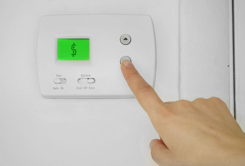 A finger lowering the heat on a thermostat.