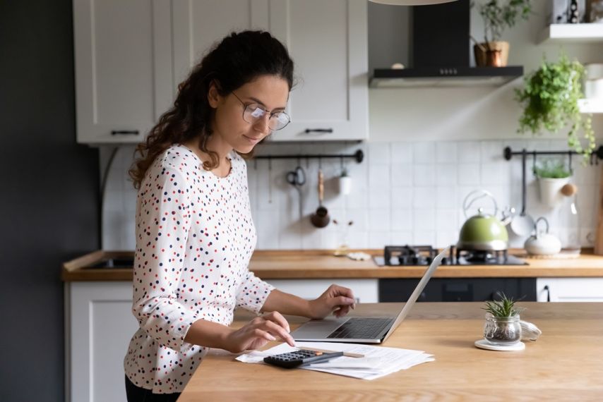 A woman working on a laptop in her kitchen.