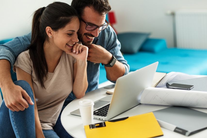 two people smile while doing taxes on a laptop