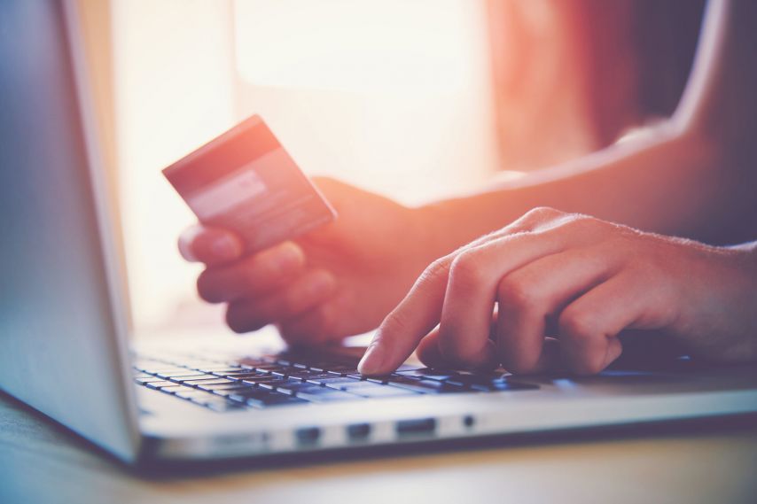 Hands using a laptop and holding a credit card.