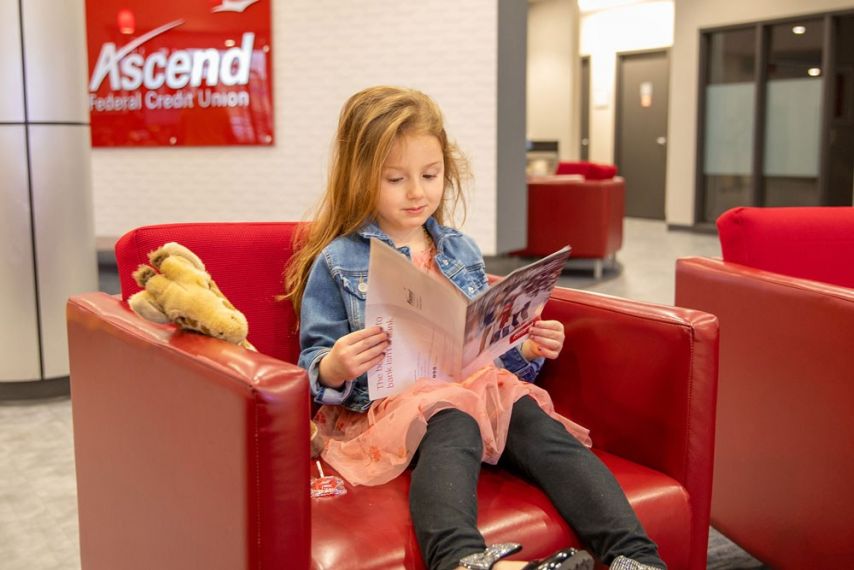 Young girl sitting inside an Ascend Federal Credit Union branch reading