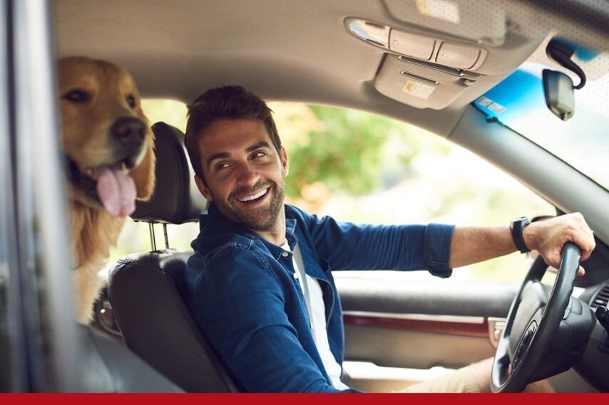 A man smiles in his car with his golden retriever beside him.