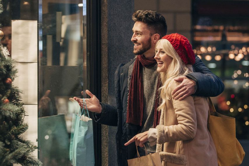 A couple looks through a window while holiday shopping.