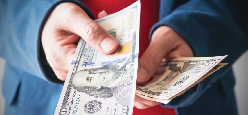 Person holding money and handing over a one hundred dollar bill