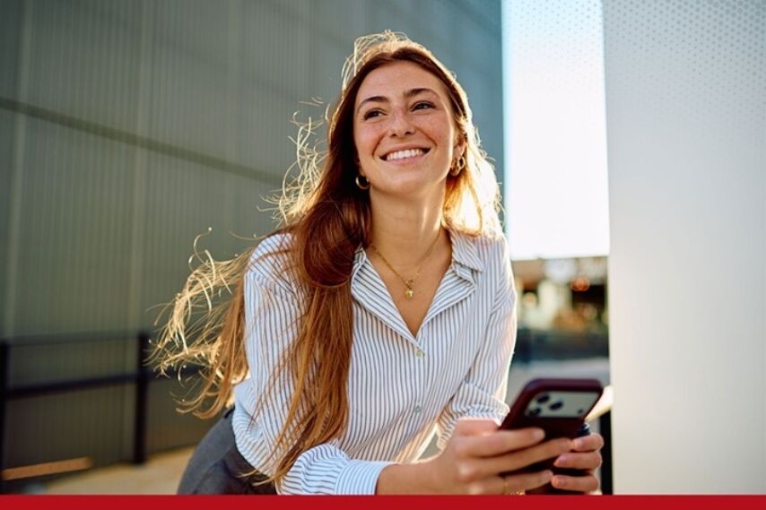 A woman looks off in the distance smiling with a phone in her hand.
