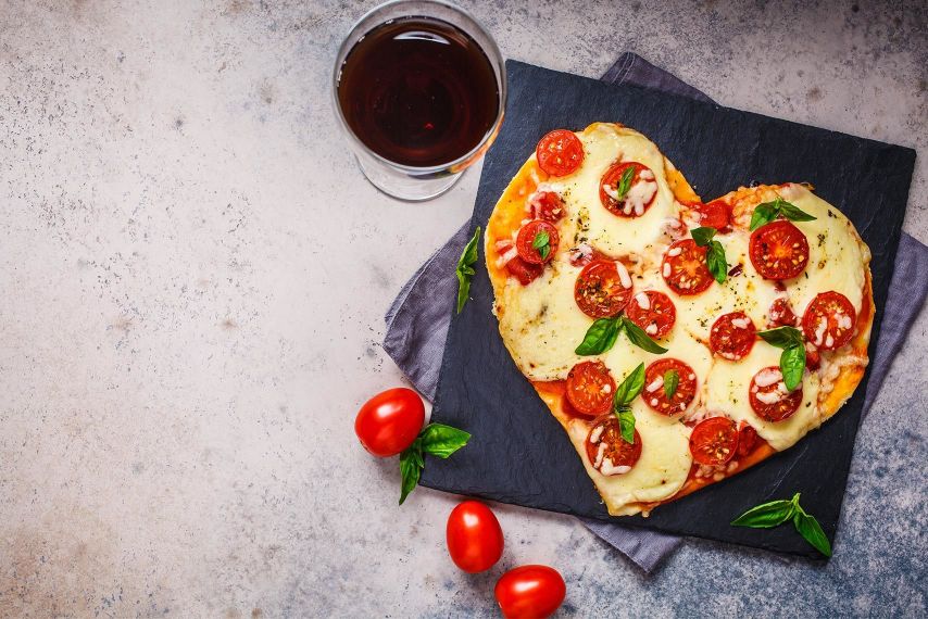 A pizza shaped like a heart with a glass of wine.