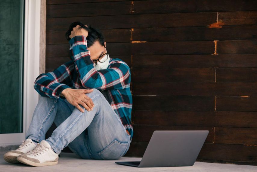 A young man wearing a mask looks at his laptop.