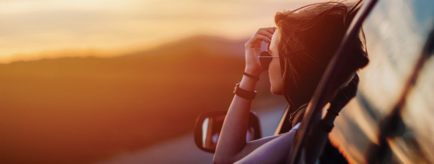 Young woman looking out of her car at sunset